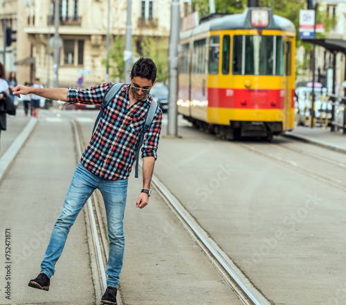 Young man walking tram rails. Hipster boy in a dressed shirt and a ranch on the back of a juggler on tram tracks.