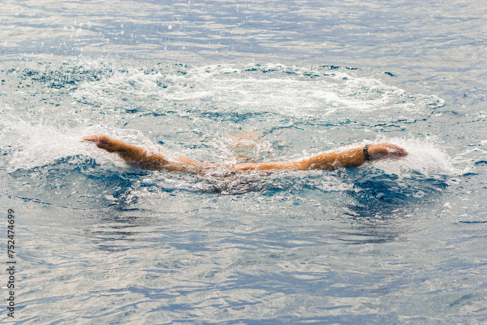 Open water swimming takes place in open bodies of water such as open oceans, lakes and rivers. A man swims in sea water, the hands of a swimmer. Sicily, Italy. Sports recreation