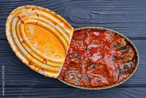 one open almina oval tin can with sardine fish in tomato sauce lies on a black wooden table photo