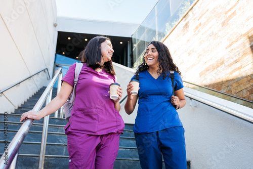 Two latin health workers women friends with scrub after work, living hospital down stairs. Nurses, medical professionals