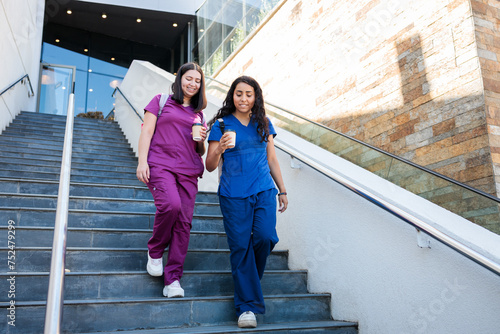 Two young latin health workers women leaving clinic or hospital. Nurses, medical professionals, down stairs with scrub