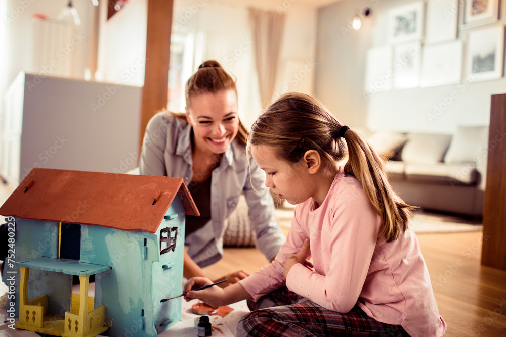 Mother and daughter painting a dollhouse together at home Mother and daughter painting a dollhouse together at home