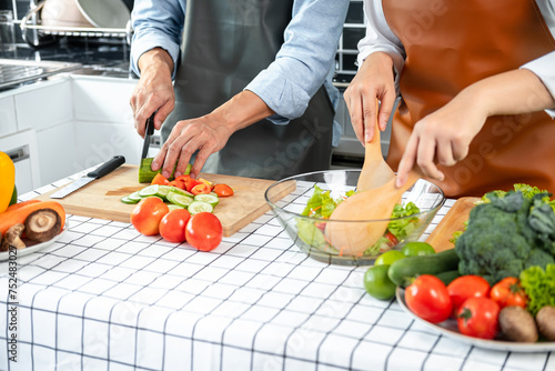 Asian romantic couple slice cucumber and tomato with knife on chopping board and holding ladle to mixing