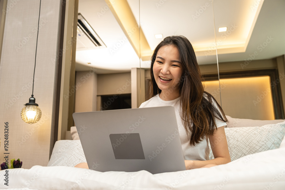 Asian woman using laptop to chatting and watching movie on social media while sitting to rest on the bed in bedroom Asian woman using laptop to chatting and watching movie on social media while sitting to rest on the bed in bedroom
