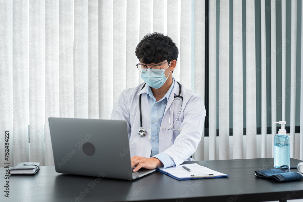 Male doctor in medical face mask using laptop to searching information about treatment the symptoms of patient Male doctor in medical face mask using laptop to searching information about treatment the symptoms of patient