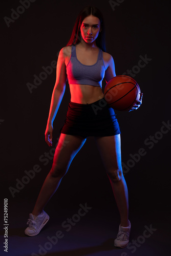 A beautiful slender girl athlete in shorts and a top plays basketball. © Dimid