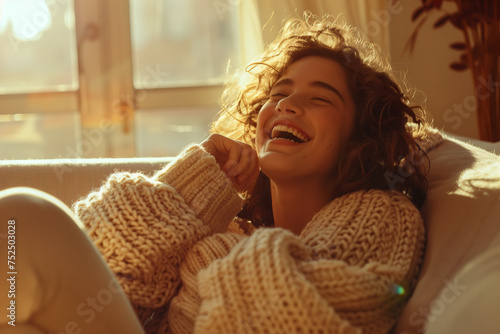 Sunlit Laughter: Woman Enjoying a Cozy Moment. A young lady wrapped in a chunky sweater laughs in sun-drenched comfort.