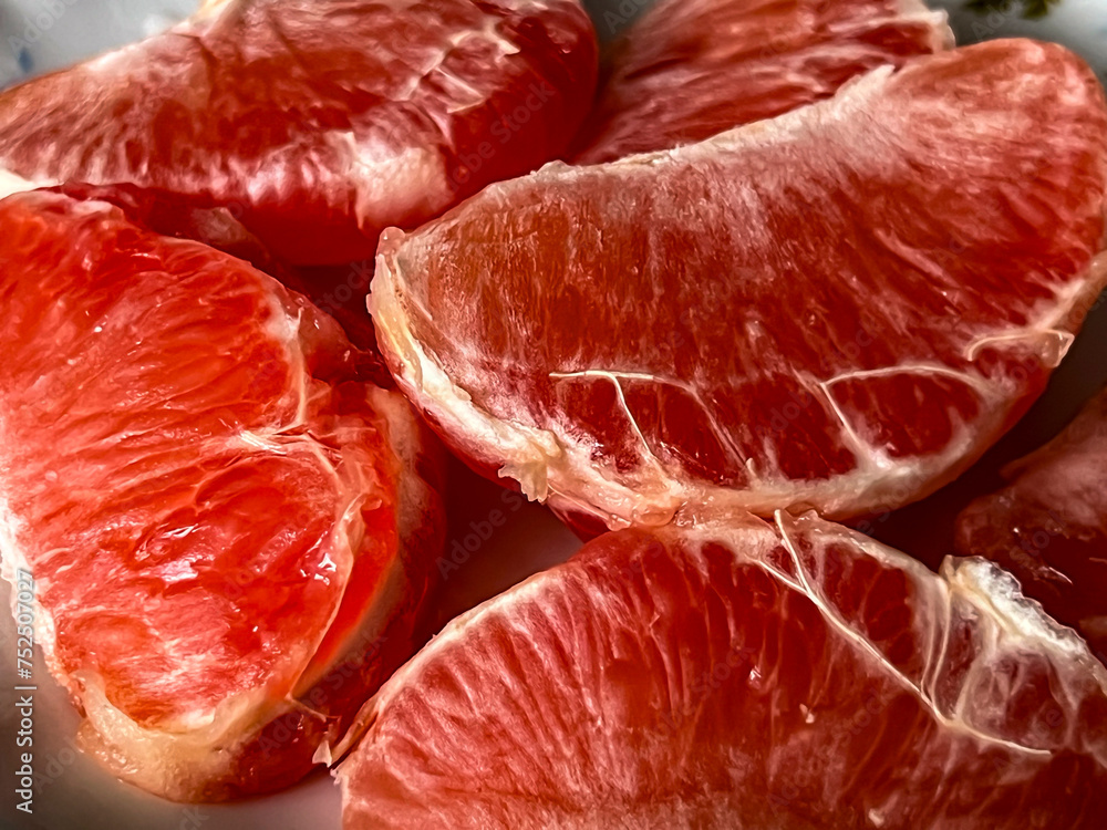 Pieces of peeled red grapefruits lying on a plate close-up