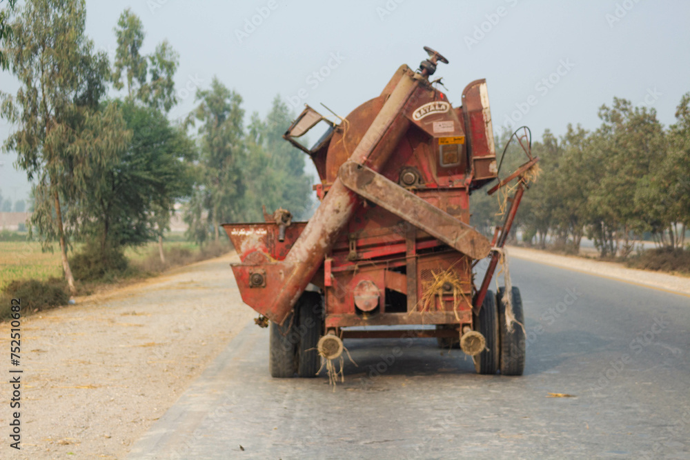 Fototapeta premium old rusty rice thresher on road with tractor