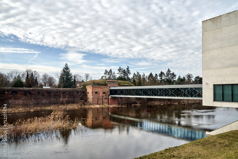 modern building, pedestrian bridge and historic defensive walls over the Warta River in Poznan - obrazy, fototapety, plakaty 