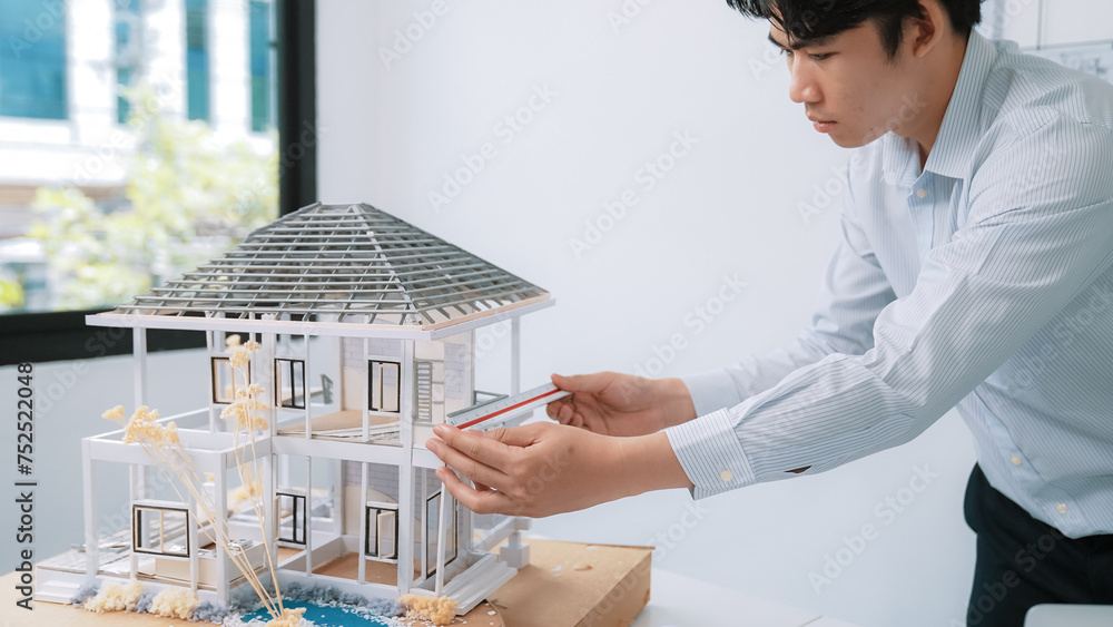 Closeup image of professional male asian architect engineer hand focusing on measure modern house model at white modern office. Focus on hand. Creative living and design concept. Immaculate.