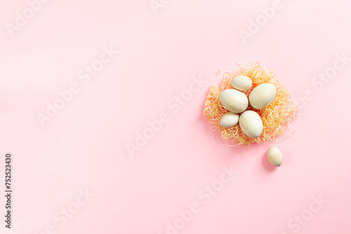 Wooden eggs lying on artificial nest on pink background. Easter eco-friendly concept