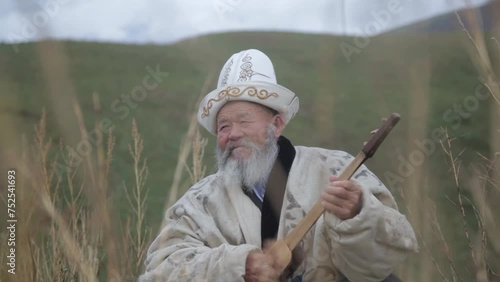 An old man in the mountains tunes and plays the Kyrgyz musical instrument komuz photo