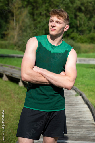 jeune homme blond en tenu de sport les bras croises dans un parc