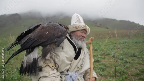 An old man in the mountains holds an eagle in his hand. A man in Kyrgyz national clothes photo