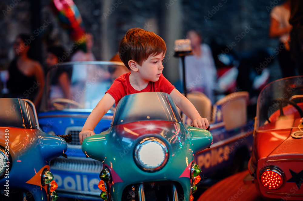 A child in a red shirt steers a colorful bumper car, surrounded by vivid lights and the blur of motion at a lively fair