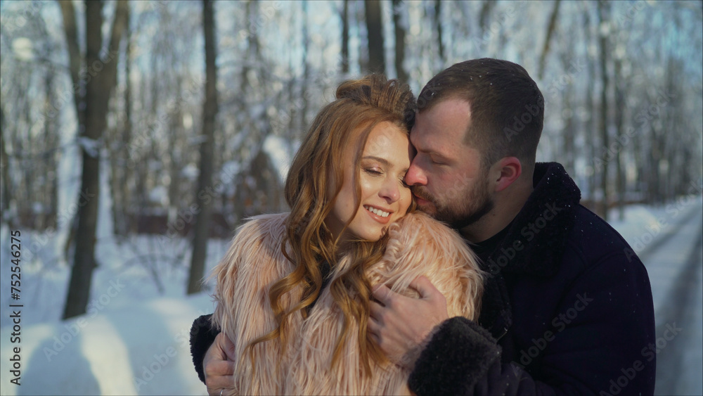 Fototapeta premium People, season, love and relaxation concept - happy couple hugging and laughing outdoors in winter. A guy and a girl hugging in a winter forest. A girl in a fur coat hugs a guy in the winter forest.