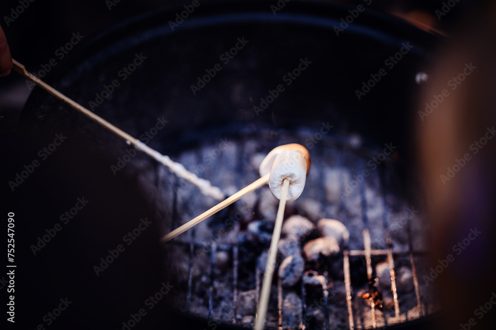 Hands carefully roast marshmallows on skewers over glowing barbecue coals, a sweet treat during outdoor activities. Hands carefully roast marshmallows on skewers over glowing barbecue coals, a sweet treat during outdoor activities.