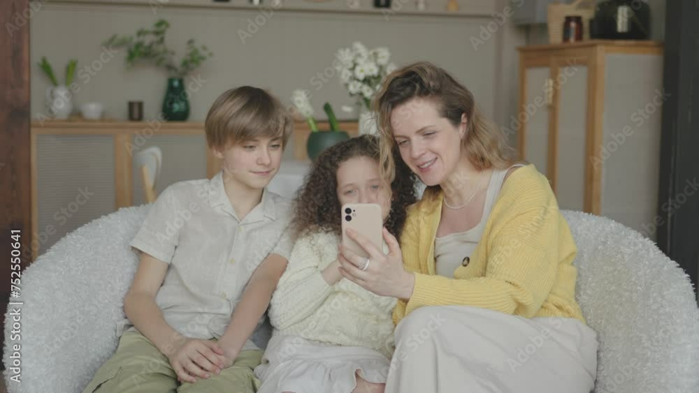 Happy family: Mother, daughter and son having fun to make selfie or video technology call to family and relatives with tablet or smartphone on sofa in living room. Family video conference Happy family: Mother, daughter and son having fun to make selfie or video technology call to family and relatives with tablet or smartphone on sofa in living room. Family video conference