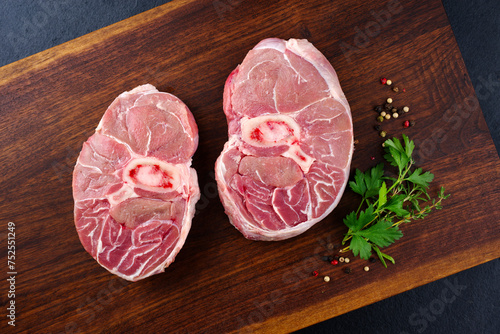 Raw beef leg slice with cross-section marbling with herbs and spices as ossobuco offered as a top view on a wooden design board