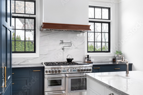 Tableau sur toile A luxurious kitchen detail with blue cabinets, a stainless steel stove, granite backsplash and countertop, and black framed windows