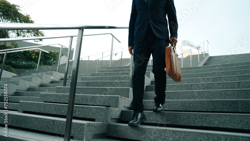 Closeup of skilled manager walking down stair with a bag and return to home. Closeup of project manager leg getting fired and walk to dormitory. Investor with untidy suit. Focus on leg. Exultant. photo