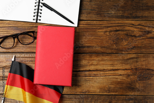 Learning foreign language. Flag of Germany, book, glasses and stationery on wooden table, flat lay with space for text