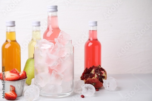 Tasty kombucha in bottles, glass with ice and fresh fruits on white table, space for text
