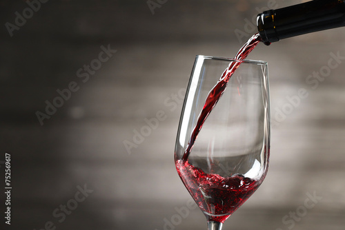 Pouring red wine into glass against gray background, closeup. Space for text