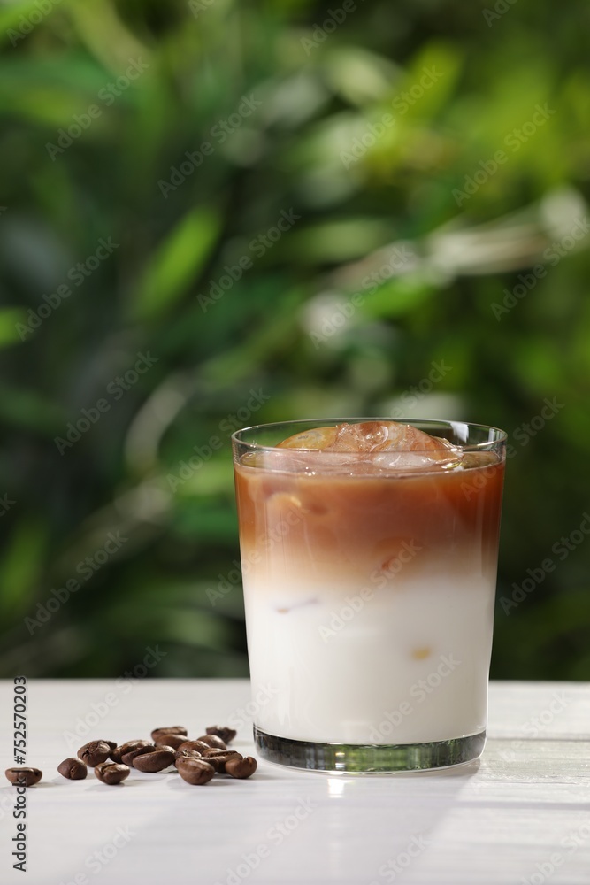 Obraz premium Glass of iced coffee and beans on white wooden table outdoors. Space for text
