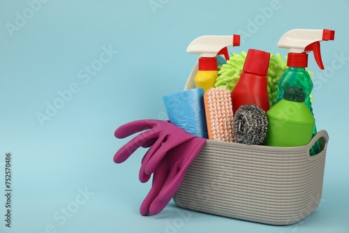 Different cleaning products in basket on light blue background, space for text