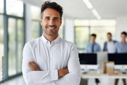 A man standing with crossed arms in an office setting. Suitable for business concepts