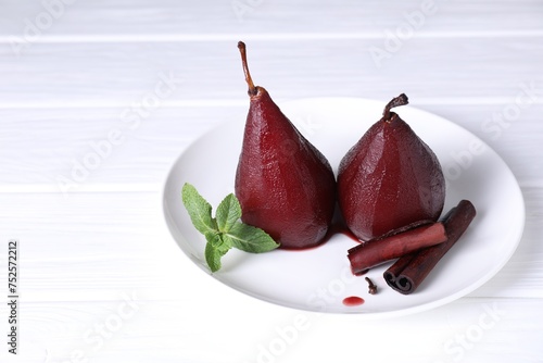 Tasty red wine poached pears with mint and cinnamon on white wooden table, closeup. Space for text