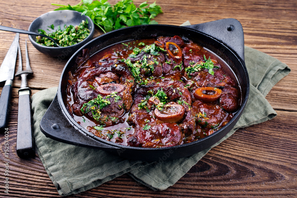 Traditional braised Italian ossobuco alla Milanese with gremolata in white wine and veal sauce served in a cast-iron design stewpot