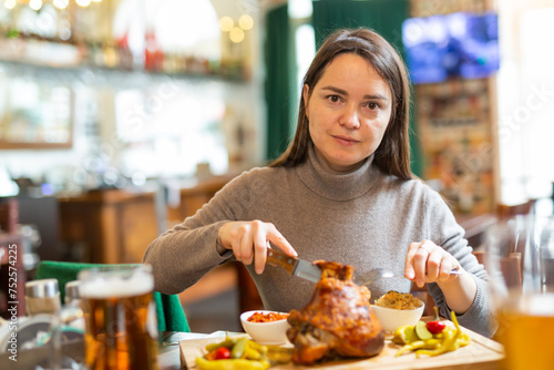 Positive brunette having lunch in Viennese cafe with traditional dish Schweinsstelze  crispy roasted ham hock with vegetable side dishes and glass of beer. Local cuisine