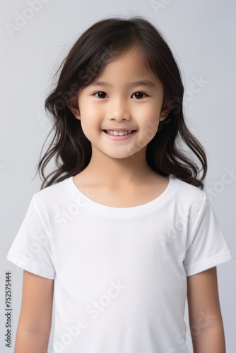 Portrait of a little Asian girl smiling at the camera in a white t shirt on a white background