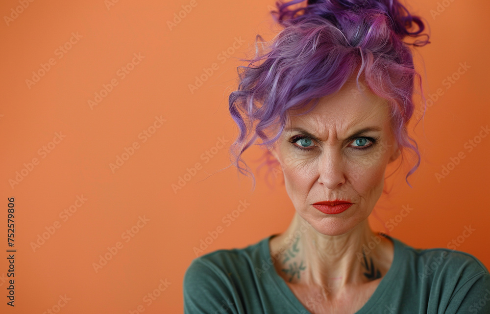 Portrait of an old angry woman 60 years old with purple hair in green clothes on an isolated peach color background. Aggression woman Portrait of an old angry woman 60 years old with purple hair in green clothes on an isolated peach color background. Aggression woman