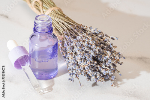 A translucent lavender-tinted glass bottle with a dropper, alongside a bunch of dried lavender flowers, evoking a sense of natural beauty and calm photo