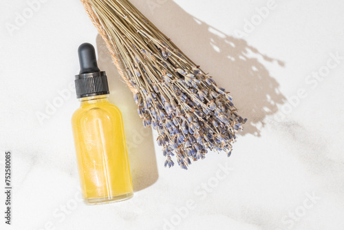 A clear bottle filled with golden-colored oil essence lies next to a bouquet of dried lavender, suggesting organic beauty and relaxation photo