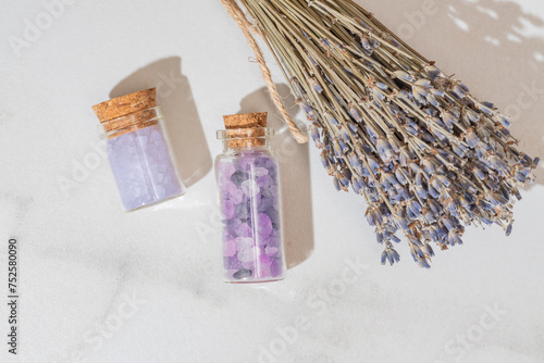 Top view of transparent glass jars with cork lids filled with purple bath salts, next to a bundle of dried lavender, embodying a tranquil spa atmosphere