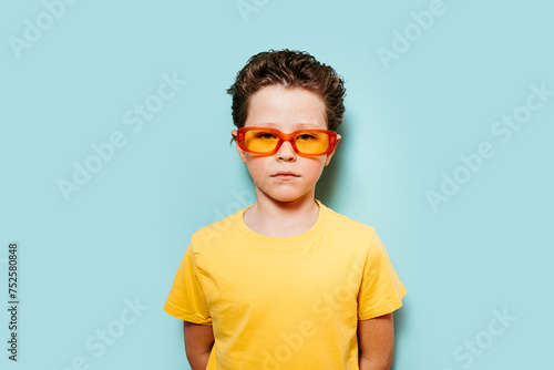 Stylish young boy with orange sunglasses against blue background photo