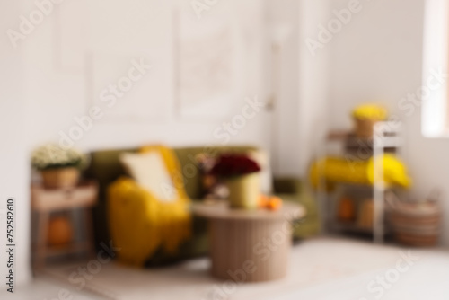 Blurred view of light living room with green sofa, chrysanthemum flowers and pumpkins on coffee table © Pixel-Shot