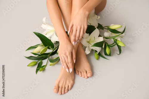 Female hands and legs with beautiful lily flowers on grey background, closeup