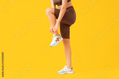Young woman in cycling shorts tying shoe laces on yellow background photo