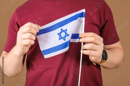 Young Jewish man with flag of Israel on brown background, closeup photo