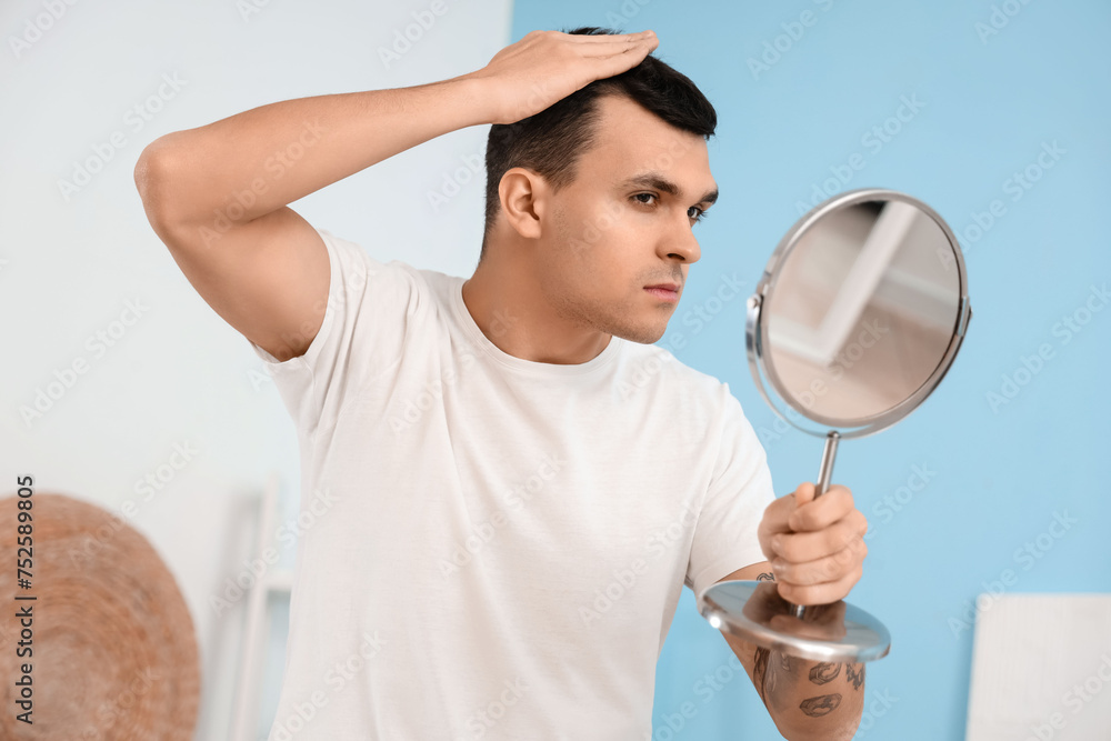 Young man with hair loss problem looking in mirror at home, closeup Young man with hair loss problem looking in mirror at home, closeup