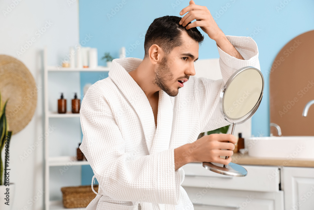 Young man with hair loss problem looking in mirror at home - obrazy, fototapety, plakaty 