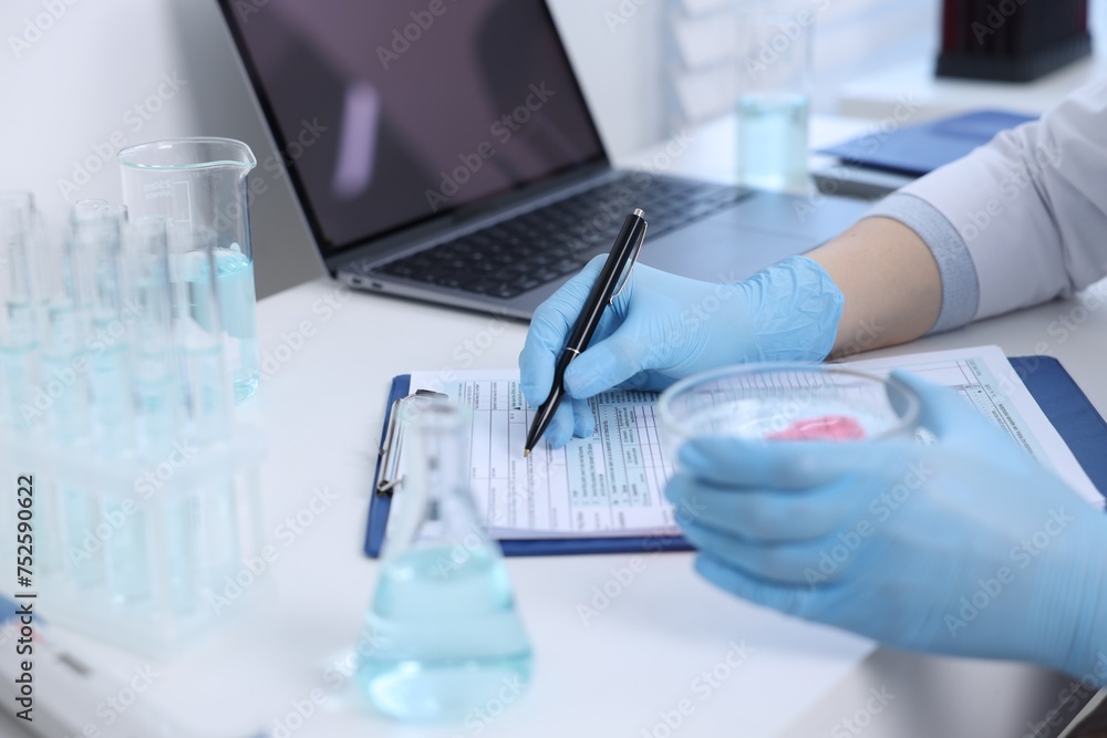 Laboratory worker holding petri dish with blood sample while working at white table, closeup Laboratory worker holding petri dish with blood sample while working at white table, closeup