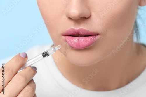 Beautiful young woman holding syringe with filler on color background, closeup