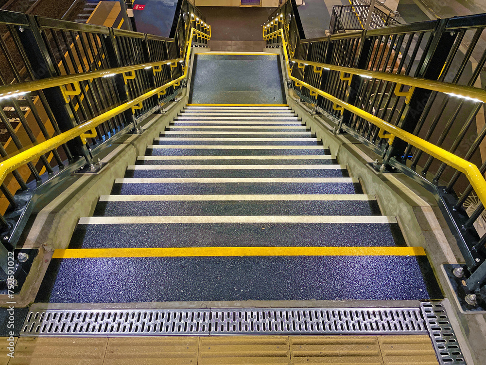 Bright yellow handrails and non-slip stairs on newly constructed staircase at UK railway station